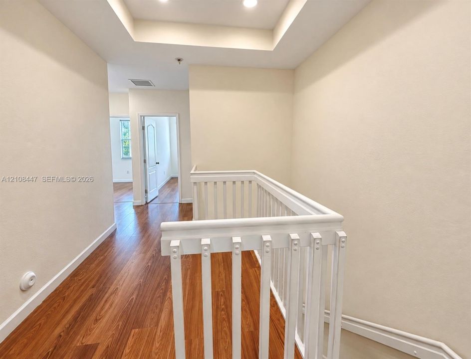 Tray ceiling featuring recessed lighting, wood-finish flooring, and white painted balustrade railing