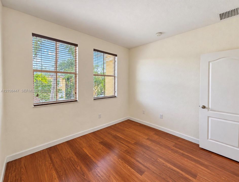 Room featuring wood-finish flooring, two windows with horizontal blinds, and a paneled interior door