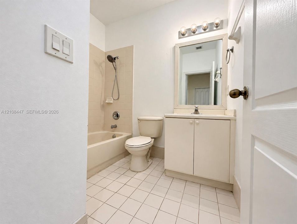 Bathroom featuring tile flooring, a tub-shower combination with tile surround, a vanity with cabinet storage, a framed wall mirror, and a multi-bulb light fixture