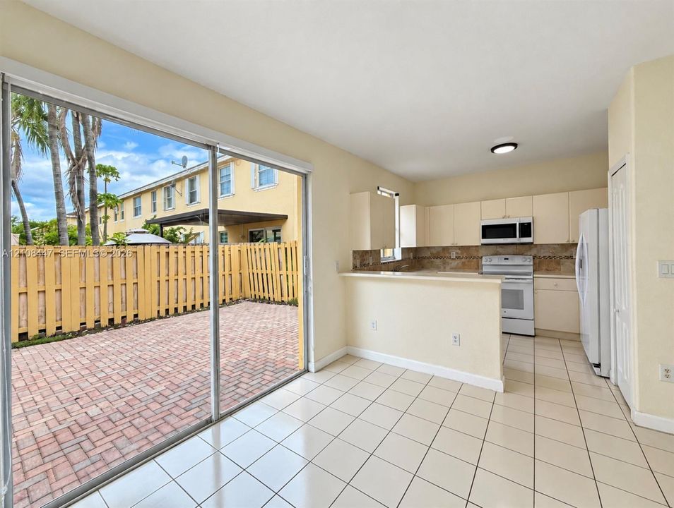 Kitchen featuring white cabinetry, an integrated microwave, and a breakfast bar, with ceramic tile flooring and sliding glass doors opening to a brick-paver patio