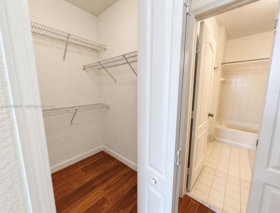 Walk-in closet featuring wire shelving and wood-finish flooring, with a bathroom showcasing ceramic tile flooring and a tub-shower combination