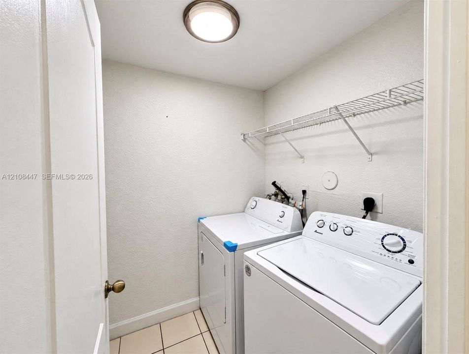 Utility area featuring ceramic tile flooring, a wall-mounted wire storage shelf, and a flush-mount overhead light fixture