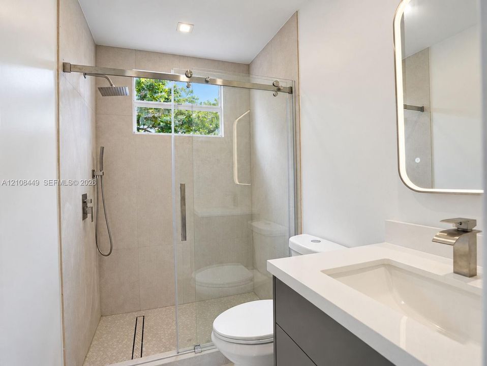Bathroom featuring a vanity with white countertop, integrated sink, and metallic faucet, complemented by an illuminated mirror