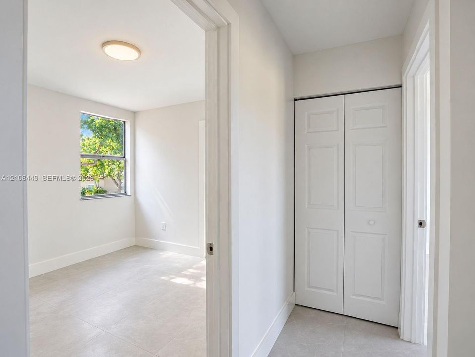 Neutral tile flooring, double-door closet with paneled detailing, window with outdoor scenery, and flush-mount ceiling lighting