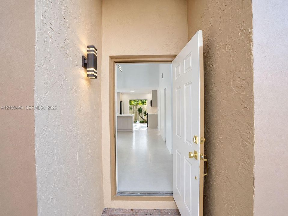 Entryway featuring a white paneled door with brass hardware, textured stucco walls, and a modern rectangular wall-mounted light fixture