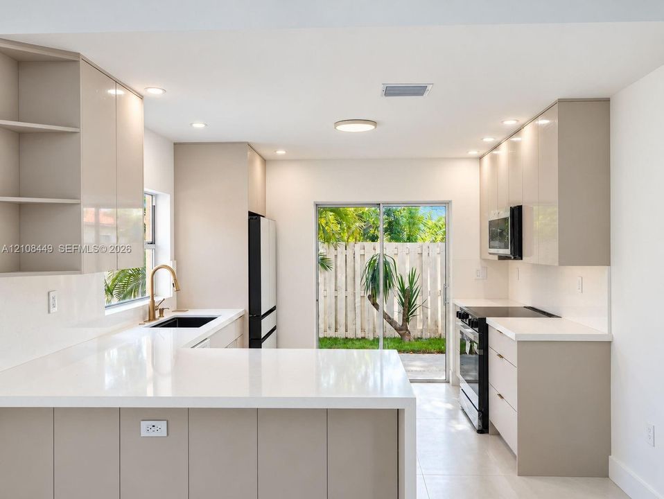 Kitchen featuring high-gloss slab cabinetry, quartz countertops, integrated under-mount sink, metallic gold-tone faucet, and recessed ceiling lighting