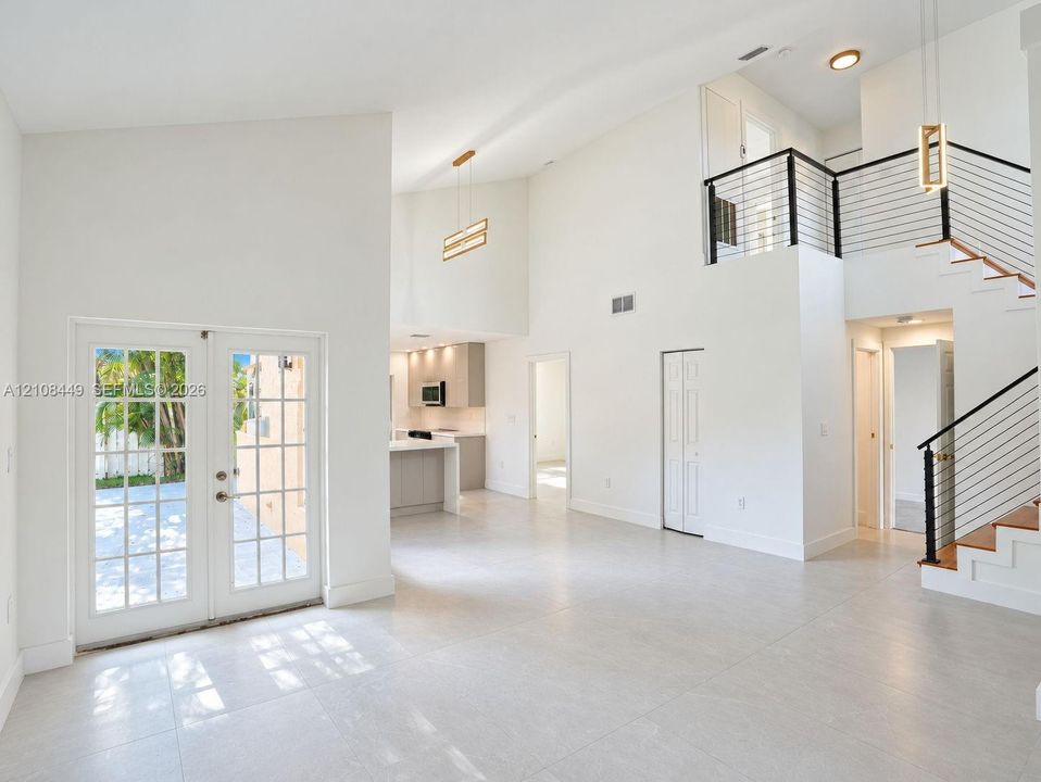 High-ceiling interior featuring tile flooring, a staircase with metal horizontal railings, French doors, and pendant lighting