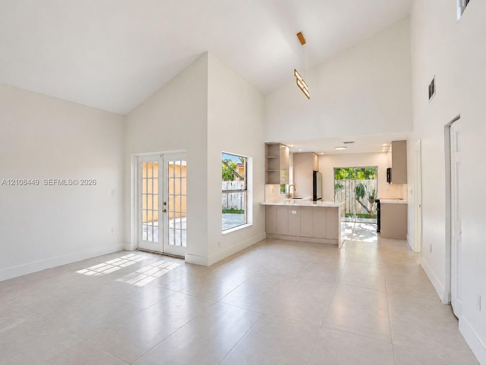 Vaulted ceilings, neutral tile flooring, kitchen peninsula with integrated cabinetry, and glass paneled French doors