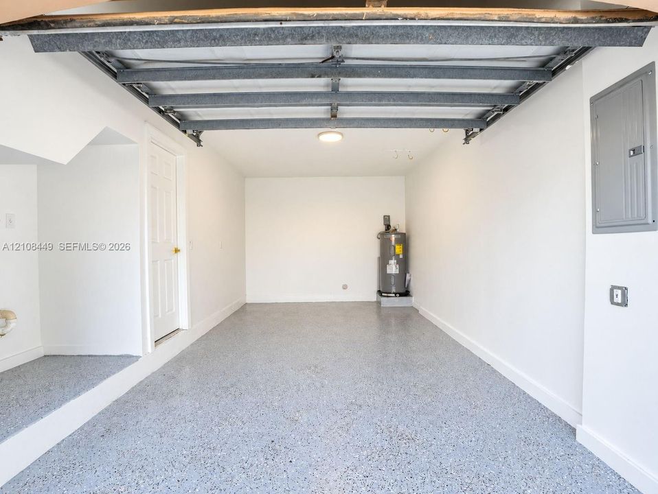 Interior garage space featuring a speckled epoxy floor coating, white walls, overhead lighting, and an integrated water heater