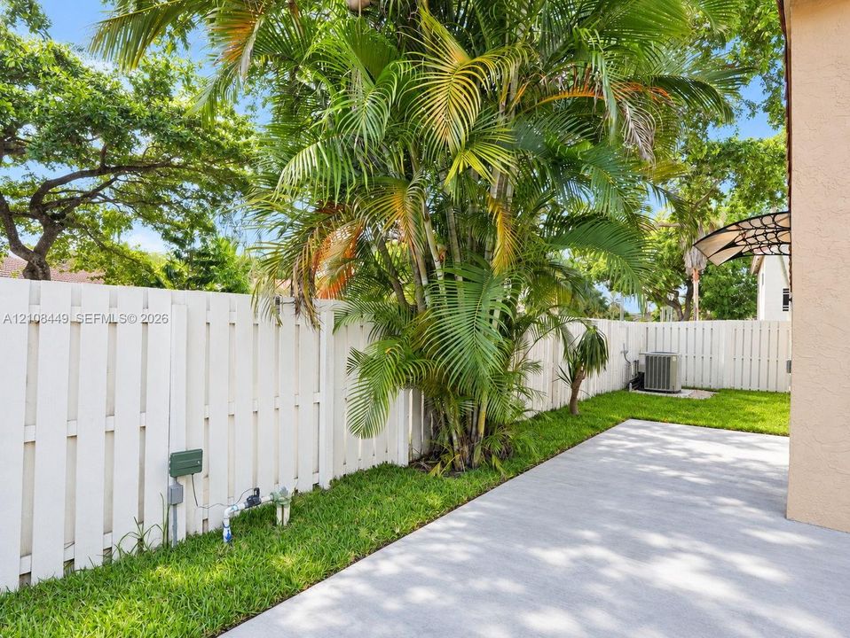 Concrete patio featuring a white privacy fence, manicured lawn, and mature palm landscaping