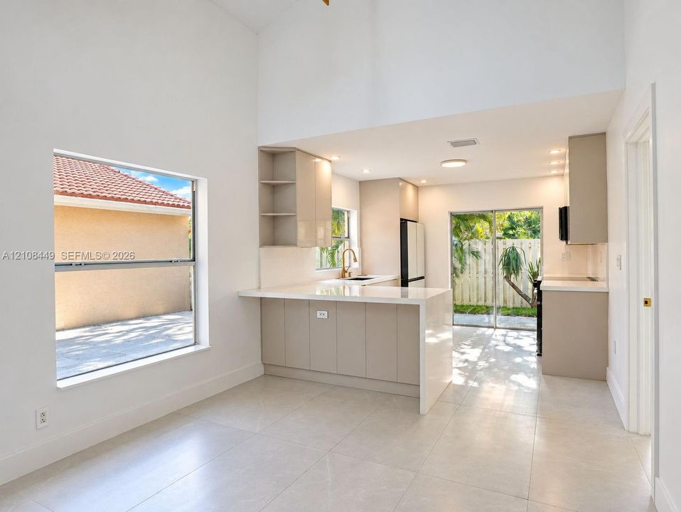 High-ceiling kitchen featuring flat-panel cabinetry, a stone-surfaced peninsula, oversized tile flooring, and sliding glass doors