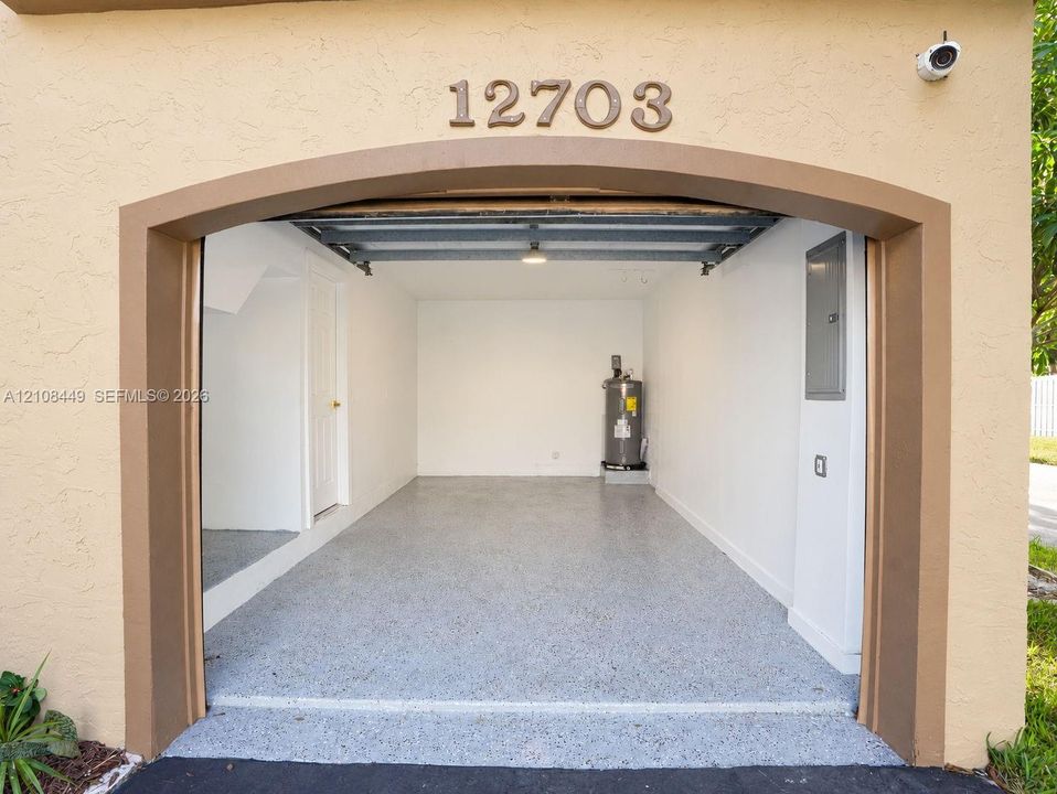 Single-car garage featuring an epoxy-coated floor, arched entry, built-in water heater, and electrical panel