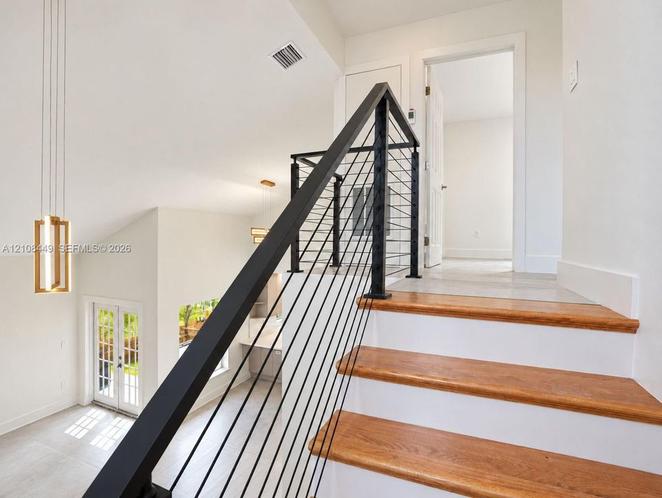 Staircase featuring wood treads, white risers, and a metal cable railing system, complemented by modern geometric pendant lighting and light-toned tile flooring