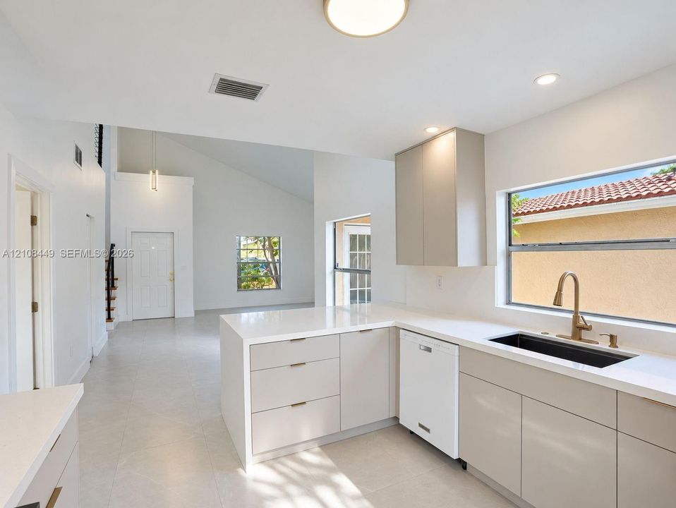 Kitchen featuring light-toned cabinetry, quartz countertops, a large undermount sink with a metallic pull-down faucet, and neutral tile flooring under high vaulted ceilings