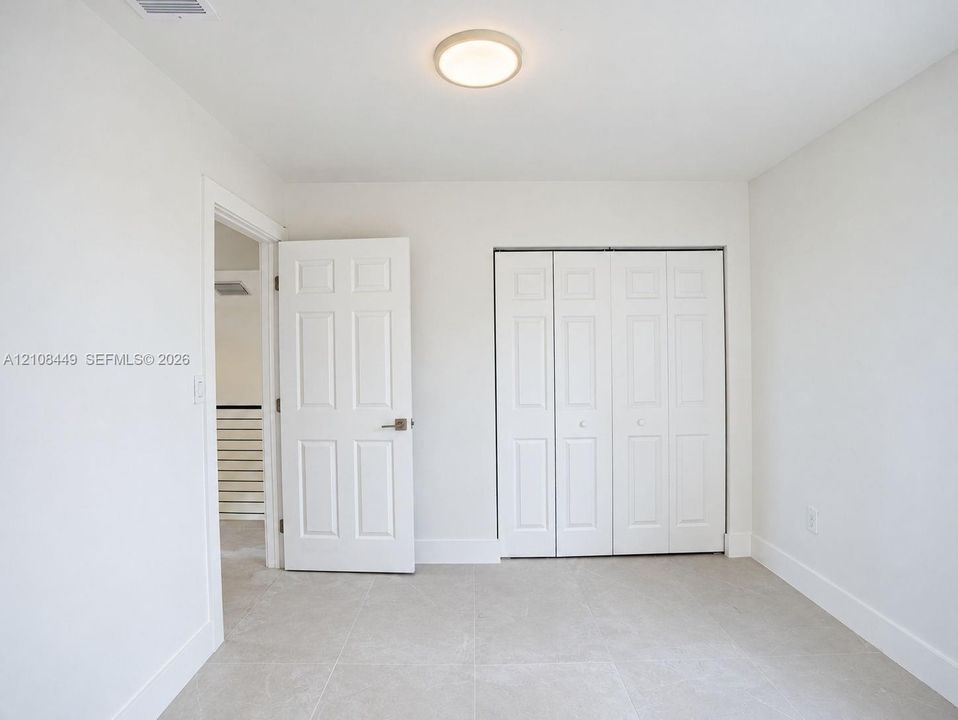 Neutral-toned tile flooring, flush-mount ceiling lighting, six-panel interior door, and a multi-panel bi-fold closet
