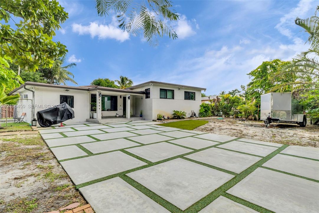 Single-story residence featuring a smooth stucco exterior, modern geometric concrete paver driveway with turf insets, and dark-framed windows