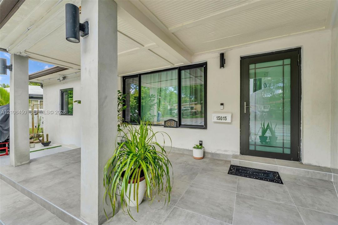Covered entryway featuring large-format gray tile flooring, a glass-panel entry door, and dark-finished exterior cylindrical wall sconces