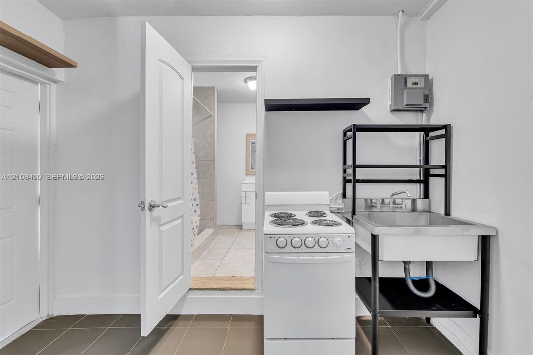 Utility space featuring dark-tone tile flooring, a white electric range, and a stainless steel basin with a metal frame