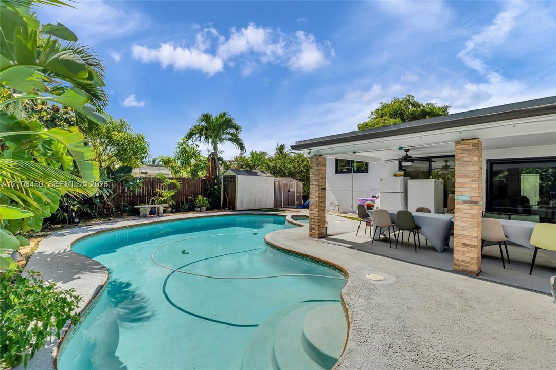 Free-form inground pool with built-in stairs, expansive concrete patio, and brick-columned covered porch