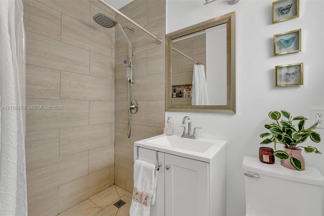 Bathroom featuring large-format neutral wall tile, rain-style showerhead, white vanity cabinet with a rectangular basin, and a framed mirror