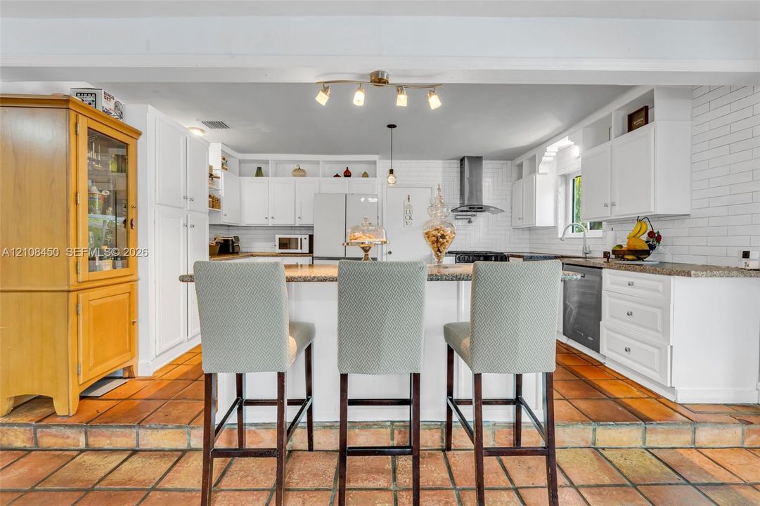 Kitchen featuring white cabinetry, stone-finish countertops, subway tile backsplash, stainless steel range hood, and tile flooring