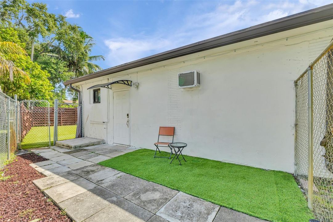Exterior space featuring painted masonry walls, concrete paver patio, synthetic turf area, and chain-link perimeter fencing