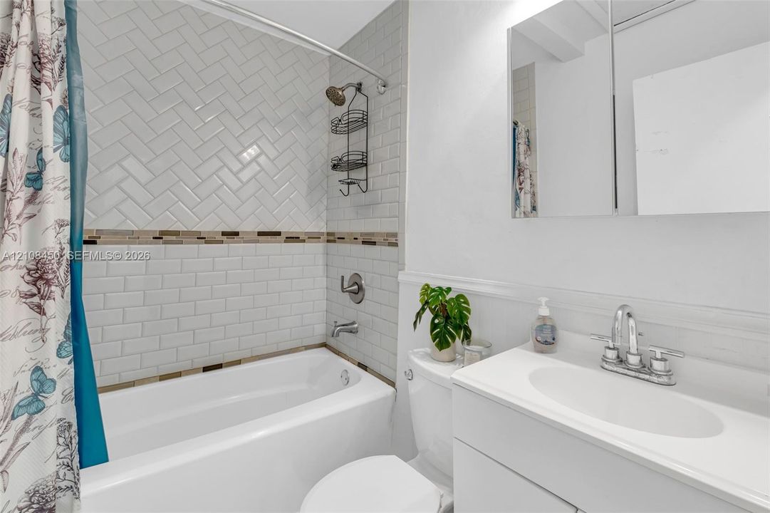 Full bathroom featuring a tub-shower combination with herringbone and subway tile surround, integrated vanity with an oval basin, and a mirrored medicine cabinet