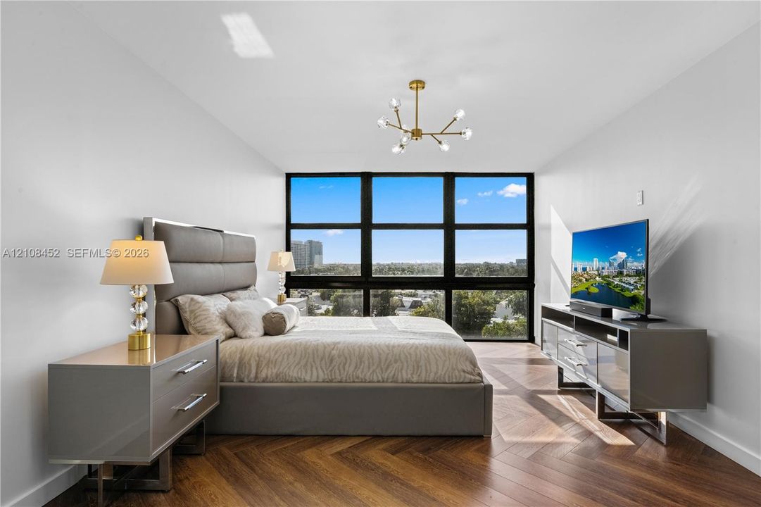 Floor-to-ceiling windows with dark framing, wood-finish herringbone flooring, and a modern multi-arm brass chandelier