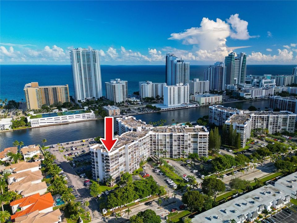 Aerial perspective of a multi-story residential building featuring wrap-around private balconies, proximity to the coastline, and waterfront positioning along a canal