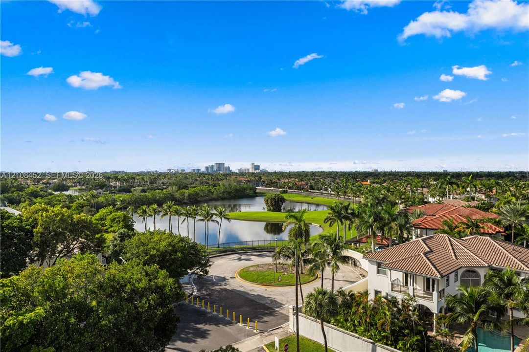 Aerial perspective featuring a tiled-roof residence, expansive water feature, mature palm trees, and panoramic cityscape horizon