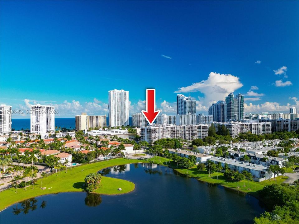 Aerial perspective of mid-rise condominium building situated on a waterfront lot featuring extensive green space and mature palm trees