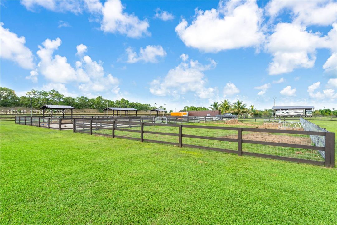 Expansive fenced pasture area featuring multiple covered structures and open-air paddocks