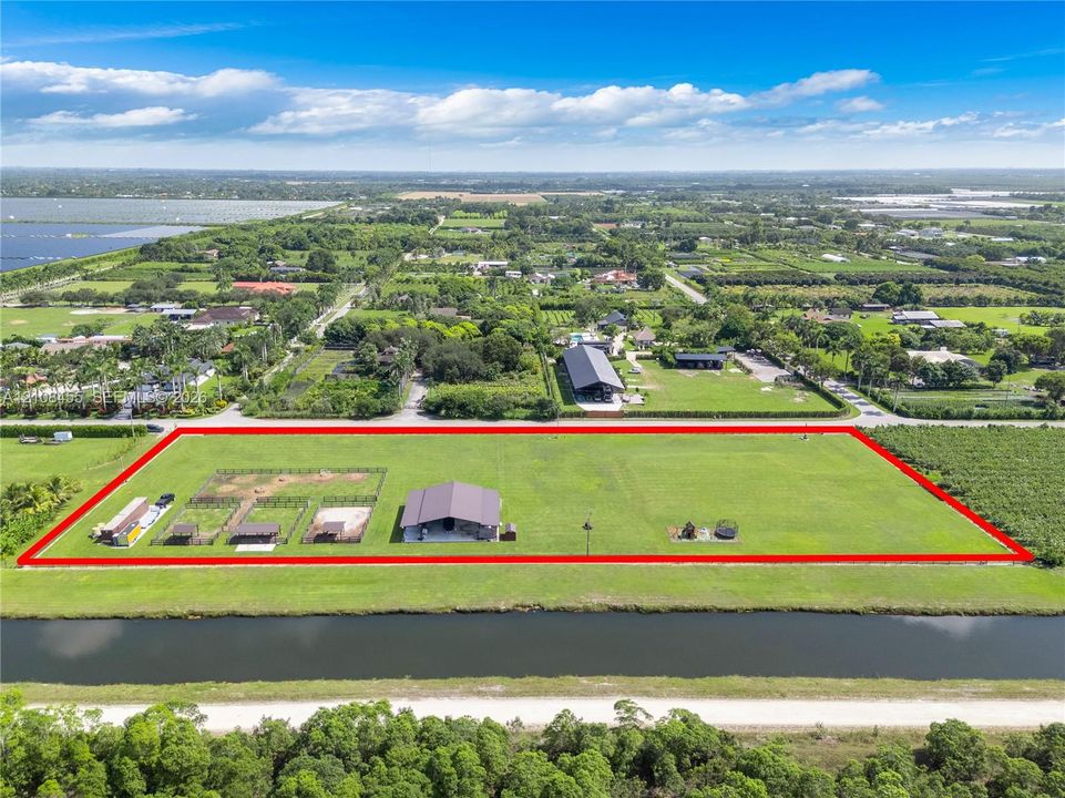 Expansive acreage featuring a metal-roof structure, dedicated animal enclosures with covered stalls, a perimeter fence, and extensive open pasture space