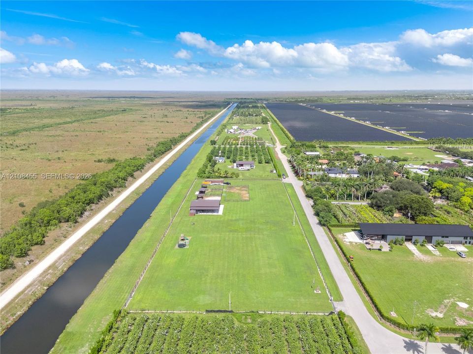 Expansive acreage featuring level pasture land, perimeter fencing, multiple detached metal structures, and direct water frontage