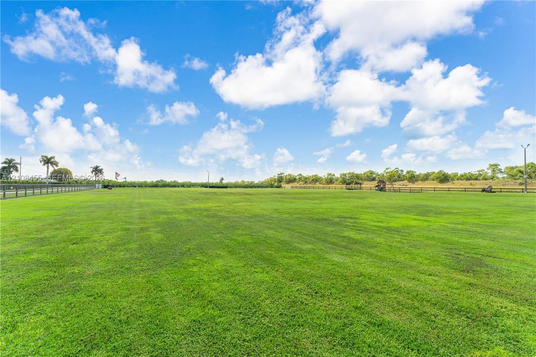 Expansive open acreage featuring manicured grass, perimeter post-and-rail fencing, and mature palm trees