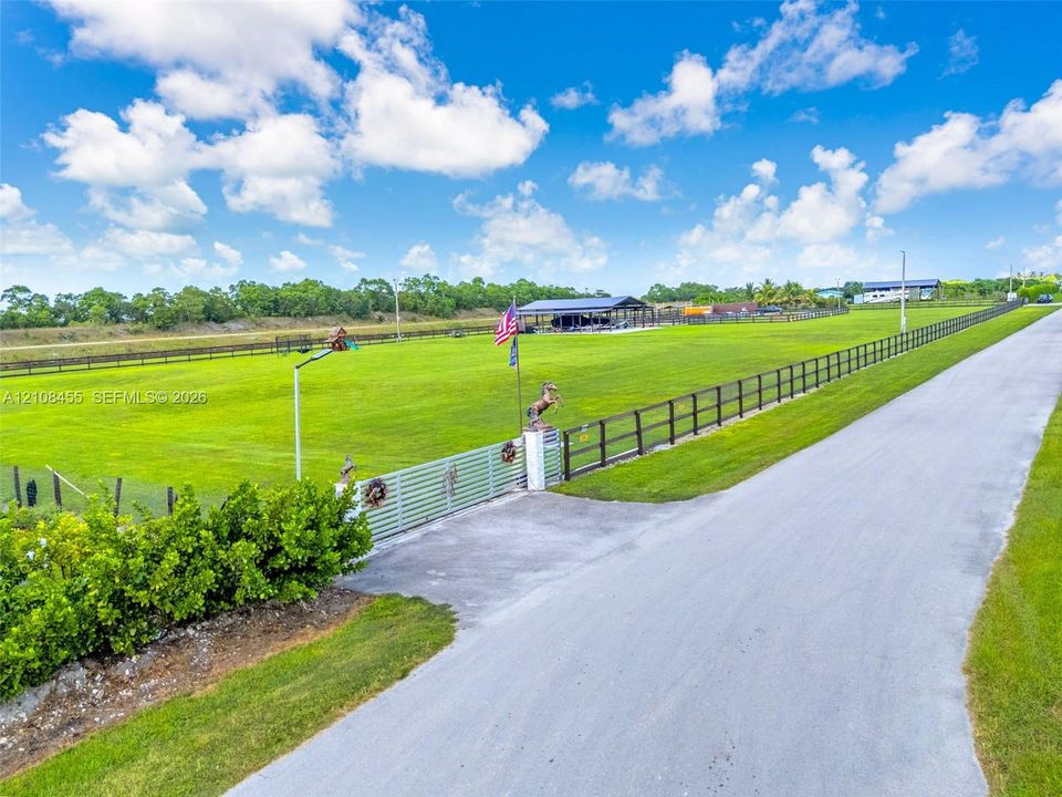 Expansive acreage featuring a paved driveway, extensive perimeter fencing, gated access, and a detached open-air structure