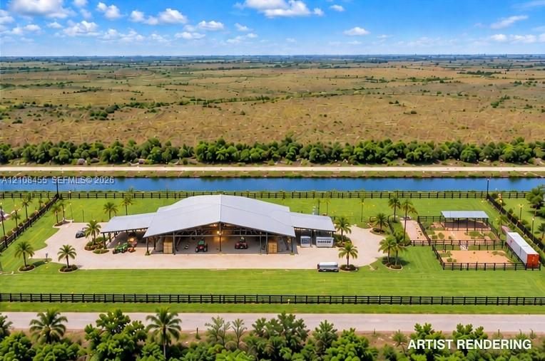 Large-scale open-air structure featuring a vaulted metal roof, paved concrete grounds, perimeter fencing, and manicured turf