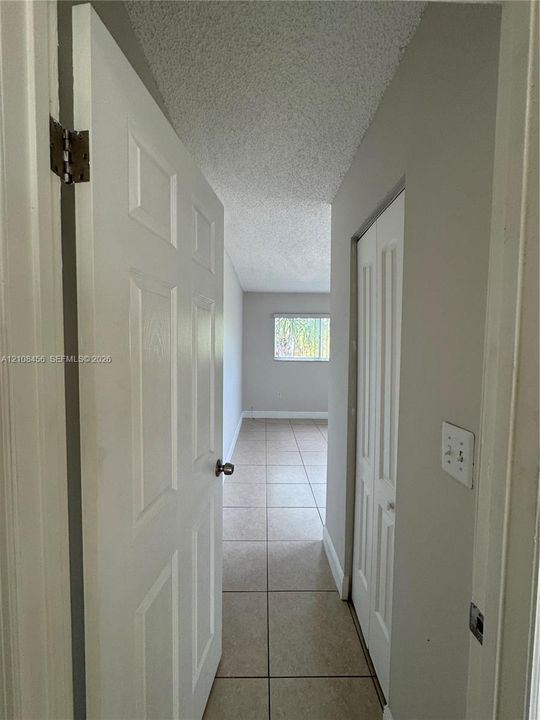 Neutral-toned interior featuring ceramic tile flooring, solid core doors, bifold closet doors, and textured ceiling finish