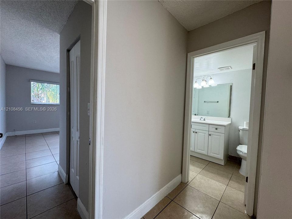 Ceramic tile flooring, white shaker-style vanity cabinet, large wall-mounted mirror, and multi-bulb vanity light fixture