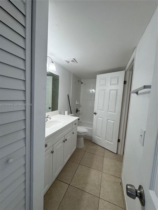 Bathroom featuring white cabinetry, an integrated sink with a polished chrome faucet, a wall-mounted mirror, ceramic tile flooring, and a shower-tub combination