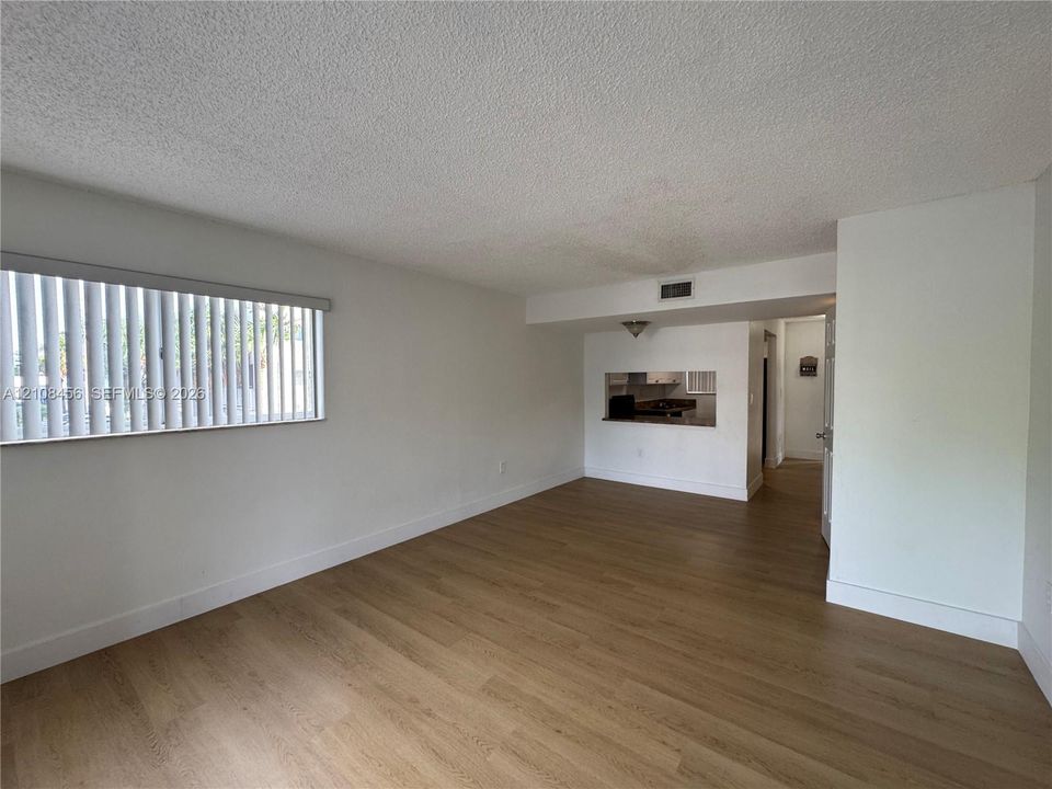 Living space featuring wood-finish flooring, vertical blinds, and a built-in kitchen pass-through