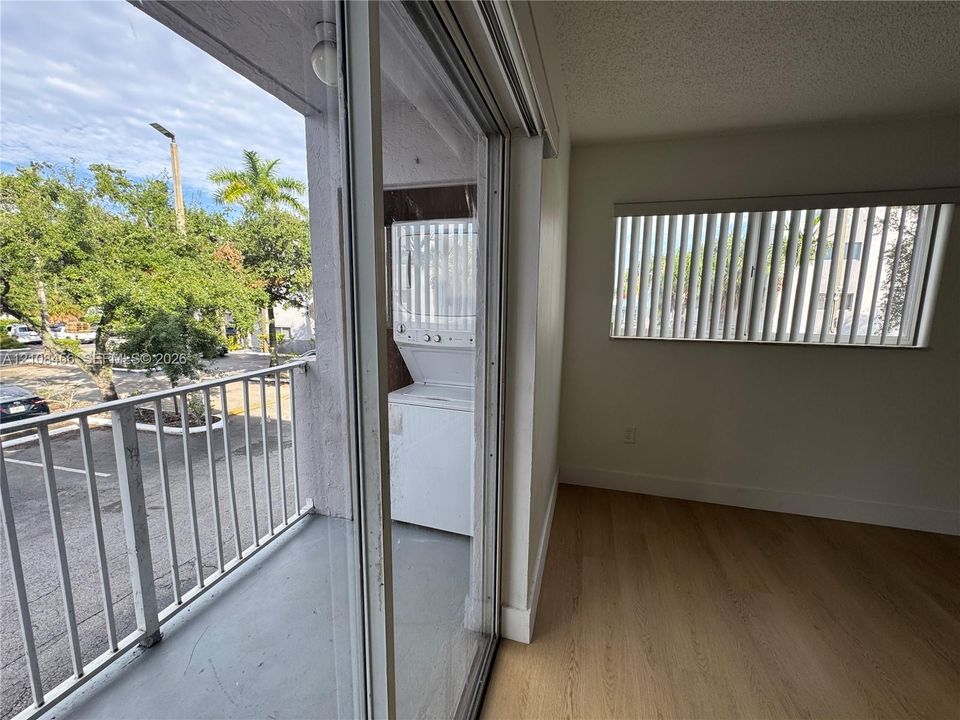 Private balcony featuring a metal railing, wood-finish flooring, integrated stackable laundry unit, and a window with vertical blinds