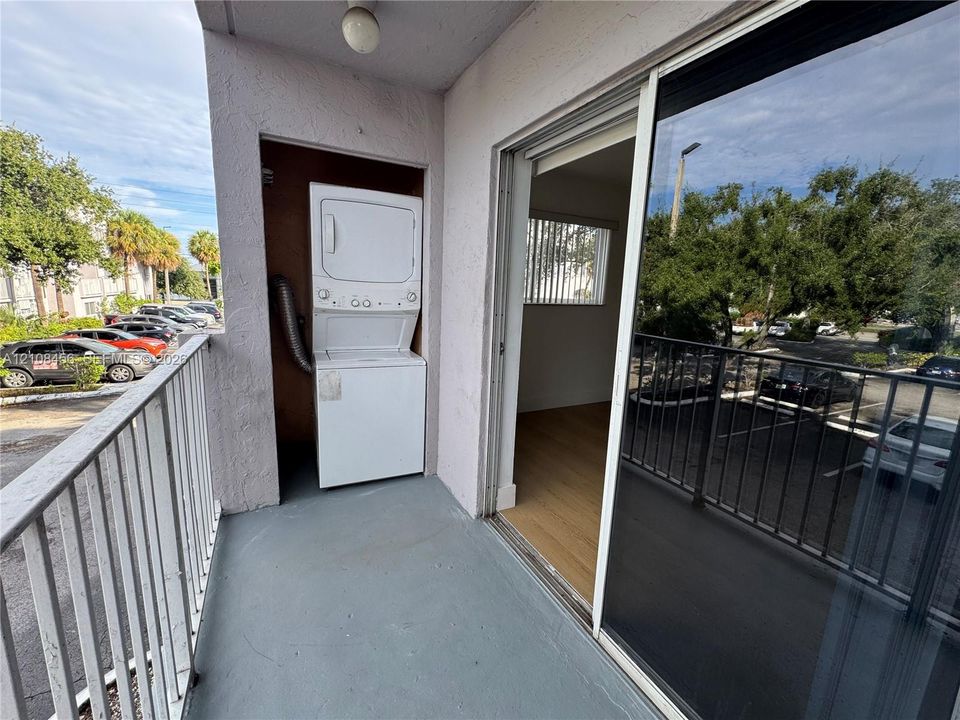 Covered balcony featuring a stacked laundry unit and metal railing