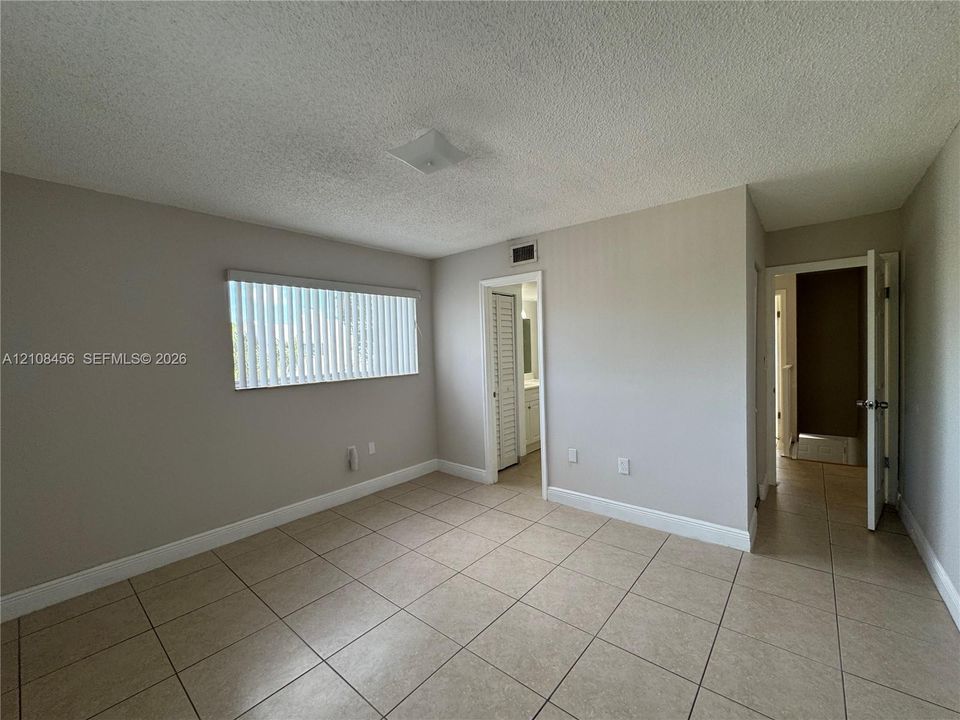 Neutral-toned interior space featuring light-colored ceramic tile flooring, a window with vertical blinds, a flush-mount ceiling light fixture, and a louvered door