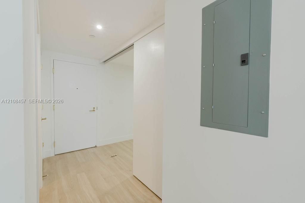 Interior entrance featuring light-toned wood-finish flooring, a solid core entry door with metallic hardware, recessed ceiling lighting, and a white sliding door