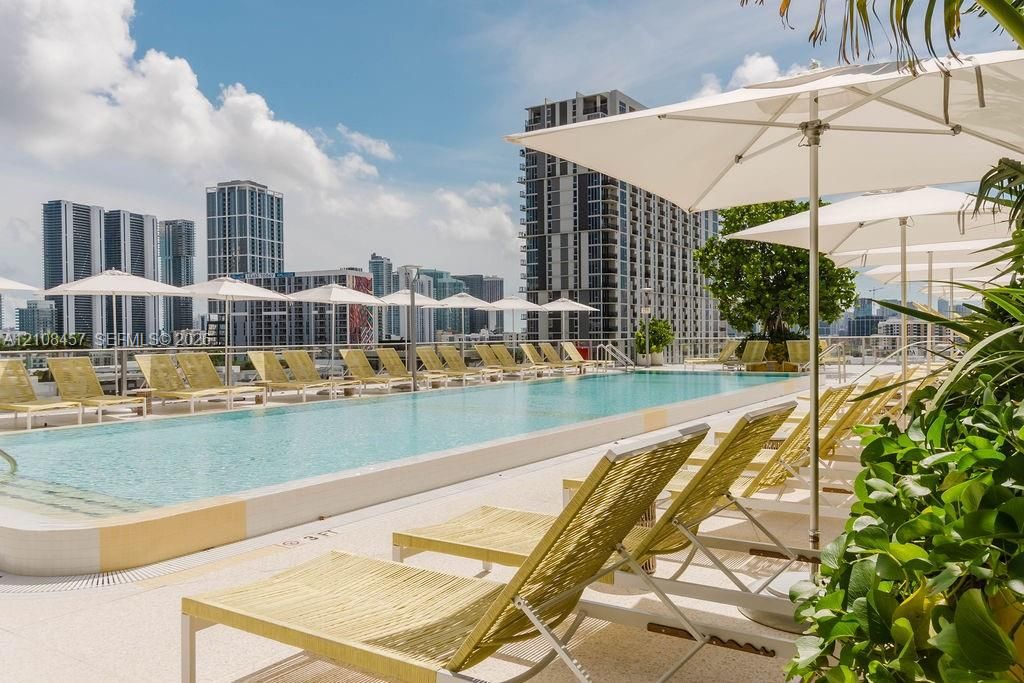 Rooftop swimming pool with a light-colored paved deck, surrounding metal railing, and integrated pool steps