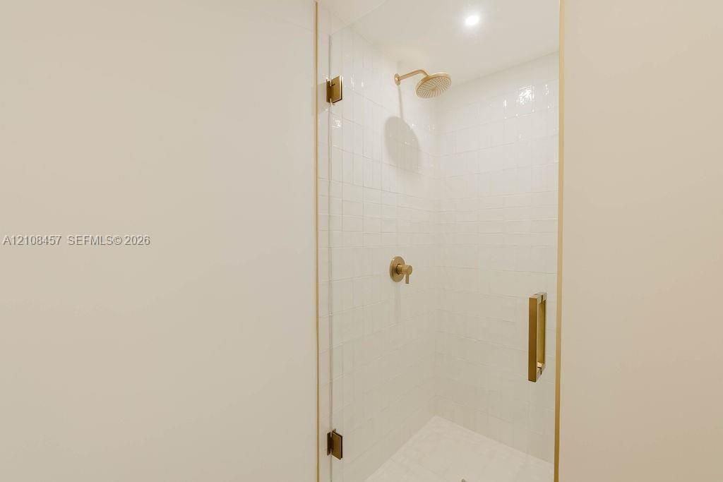 Walk-in shower featuring a frameless glass door, white wall tiling, metallic finish hardware, and a fixed shower head