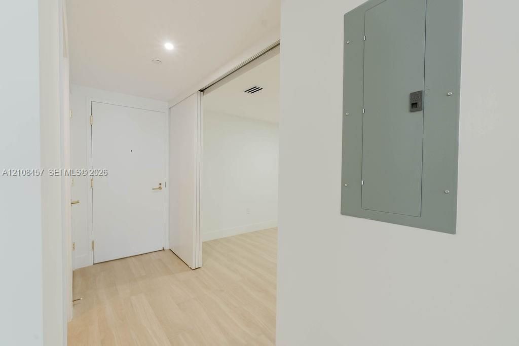 Interior entry featuring light-toned wood-finish flooring, recessed ceiling lighting, a solid-core door with metallic hardware, and an integrated electrical service panel