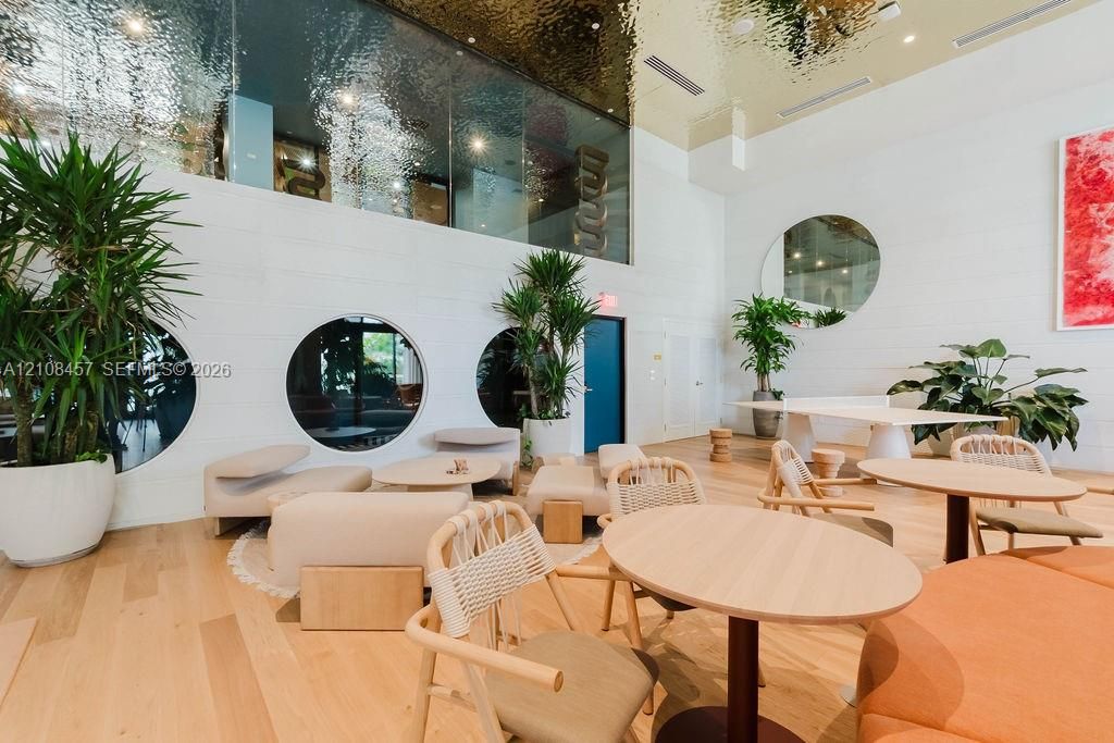 Expansive common area featuring high ceilings with a metallic finish, light wood-finish flooring, circular windows, and a large round wall mirror