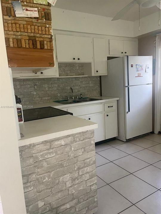 Kitchen featuring white cabinetry, brick-pattern backsplash and peninsula base, ceramic tile flooring, and a stainless steel double-basin sink